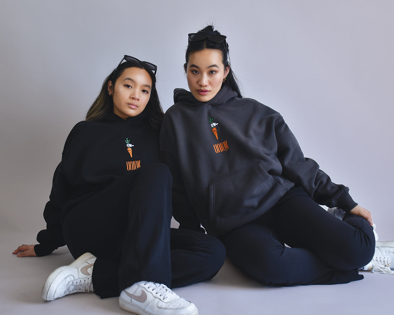 UNIQK 600 gsm Carrot Hoodie Black and Grey 100% Cotton Fleece Back Oversized Female Model sitting on Ground Front Embroidered Logo